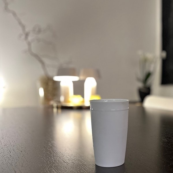 Weiße Kaffeetasse auf Holztisch, im Hintergrund: 2 Tischleuchten