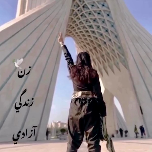 Eine Frau ohne Hijab vor dem Freiheitsturm in Teheran mit Siegeszeichen erhobener Hand.